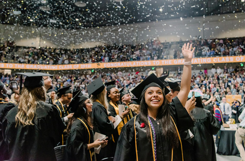 Students cheering during their graduation ceremony, confetti falling